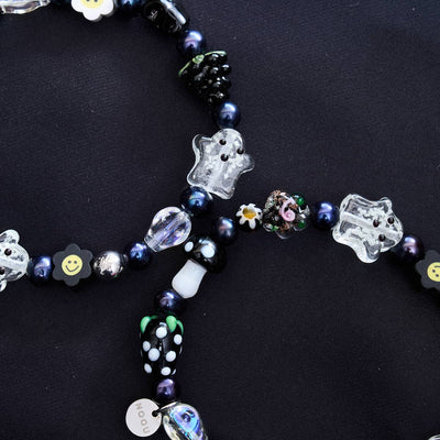 NOGU Gothic Glimmer beaded necklace with clear ghost charms, glossy black pearls, mushroom beads, and smiling flower accents.