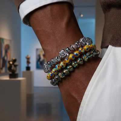NOGU MoMA Art Collection stacked bracelets with silver heart beads, yellow floral glass, and dark teal speckled beads.