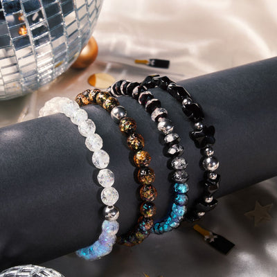 NOGU New Year Sparkle beaded bracelets in clear, black, silver, gold, and iridescent blue shimmer beside a disco ball.