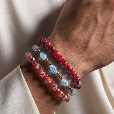 NOGU The Red Edit bracelets layered on a wrist, featuring red crystal beads, blush glass beads, blue accents and silver-tone details.
