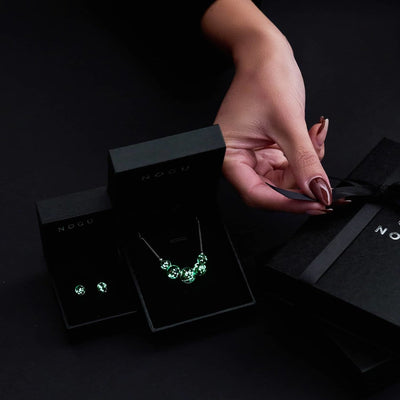 NOGU Firefly Glass Top 10 collection with luminous green stud earrings and a silver-tone beaded necklace in gift boxes.