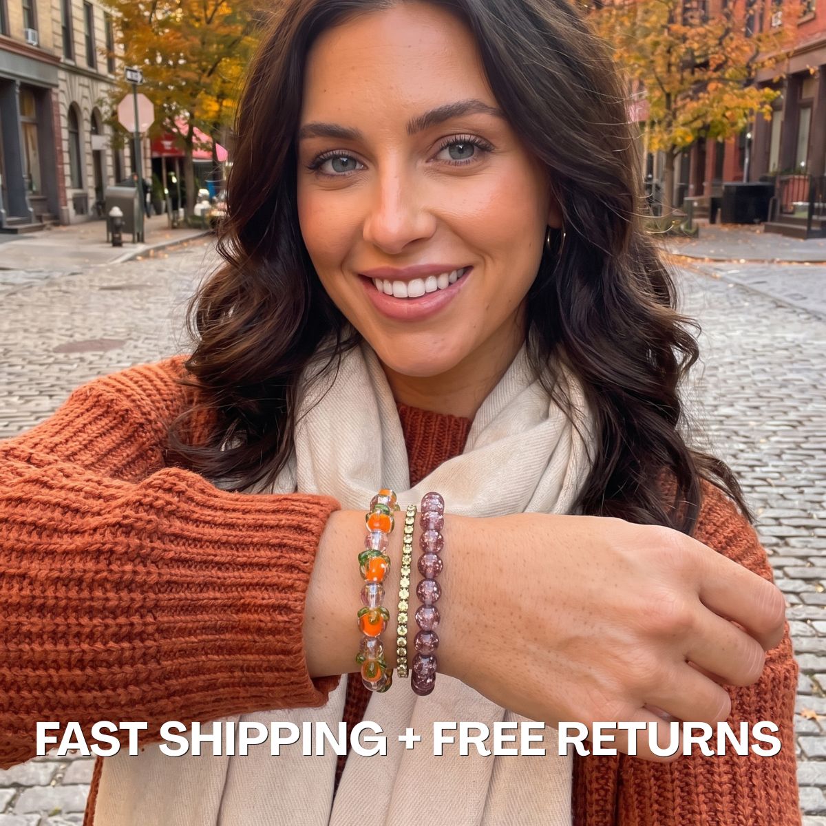 Woman wearing stacked beaded bracelets in orange, purple and gold tones with an autumn street backdrop.