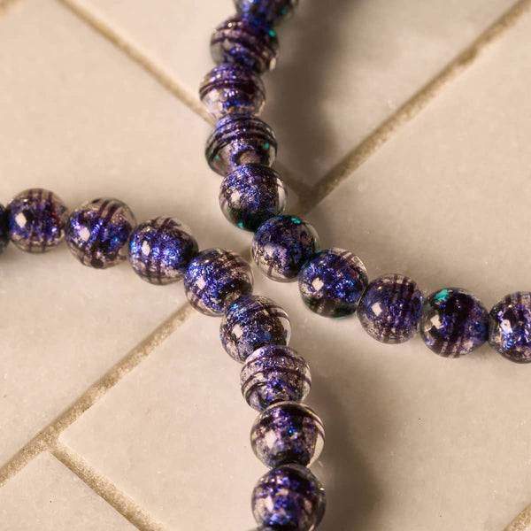 Midnight Sapphire Firework Glass Orbit bracelet with round deep blue and purple glittering glass beads on clear elastic cord.