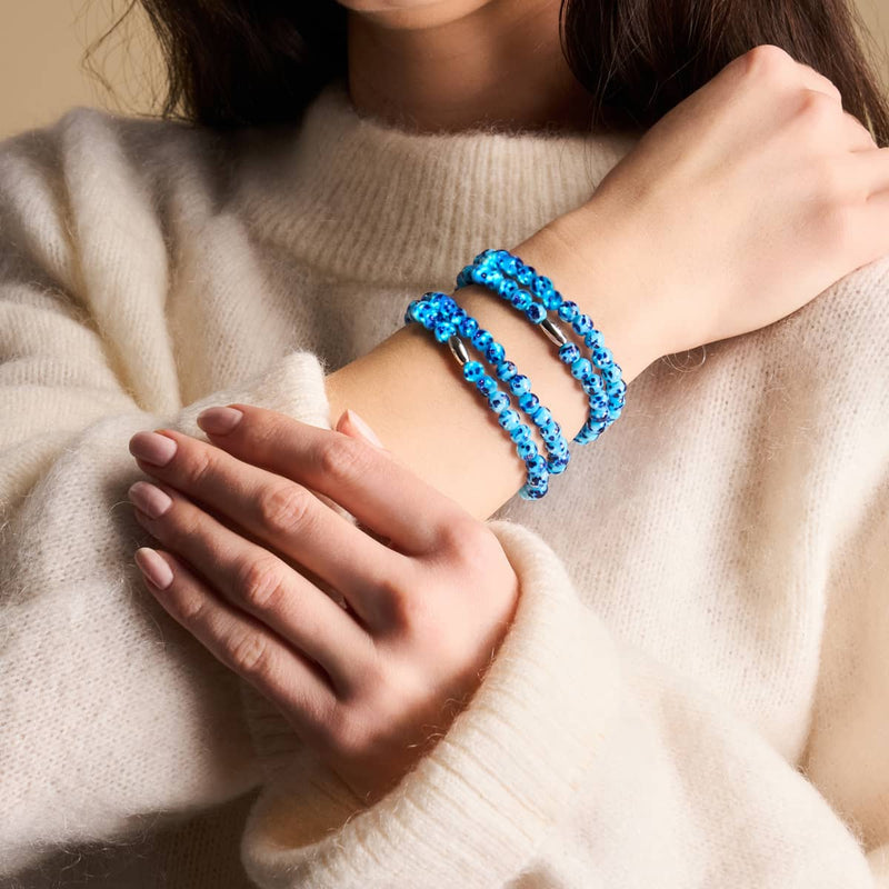 ブルー・シースプレーFirefly Glassラップブレスレットで、スターリングシルバーに6mmの青いビーズが入り、NOGUが手首に着用しています