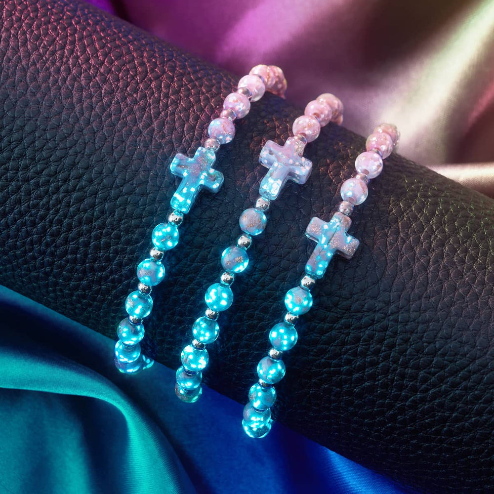 Periwinkle Firefly Glass Cross Bracelets with glowing glass beads and stainless steel accents displayed on black textured surface by NOGU